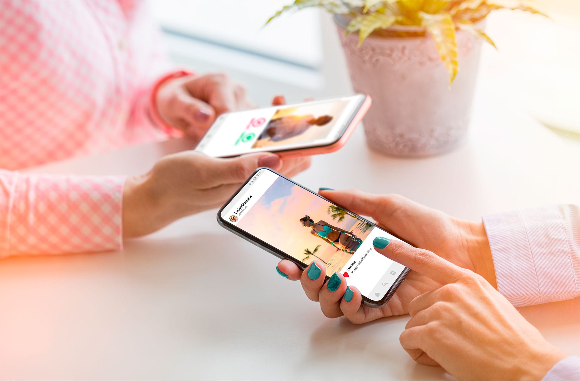 Hand of two women holding their smartphones on a table while browsing photo and video sharing social media networks